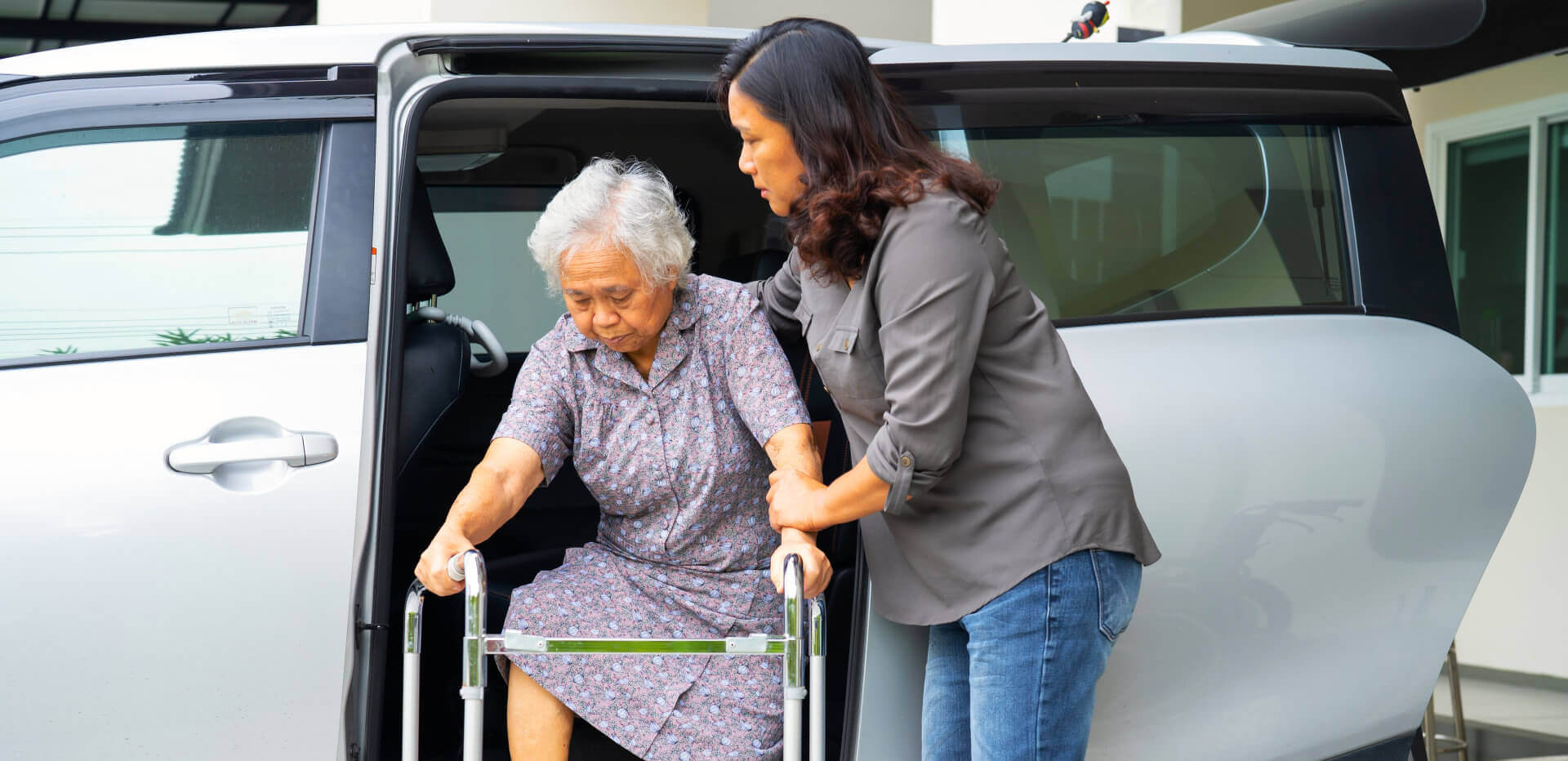 woman assisting an elderly woman get off the car