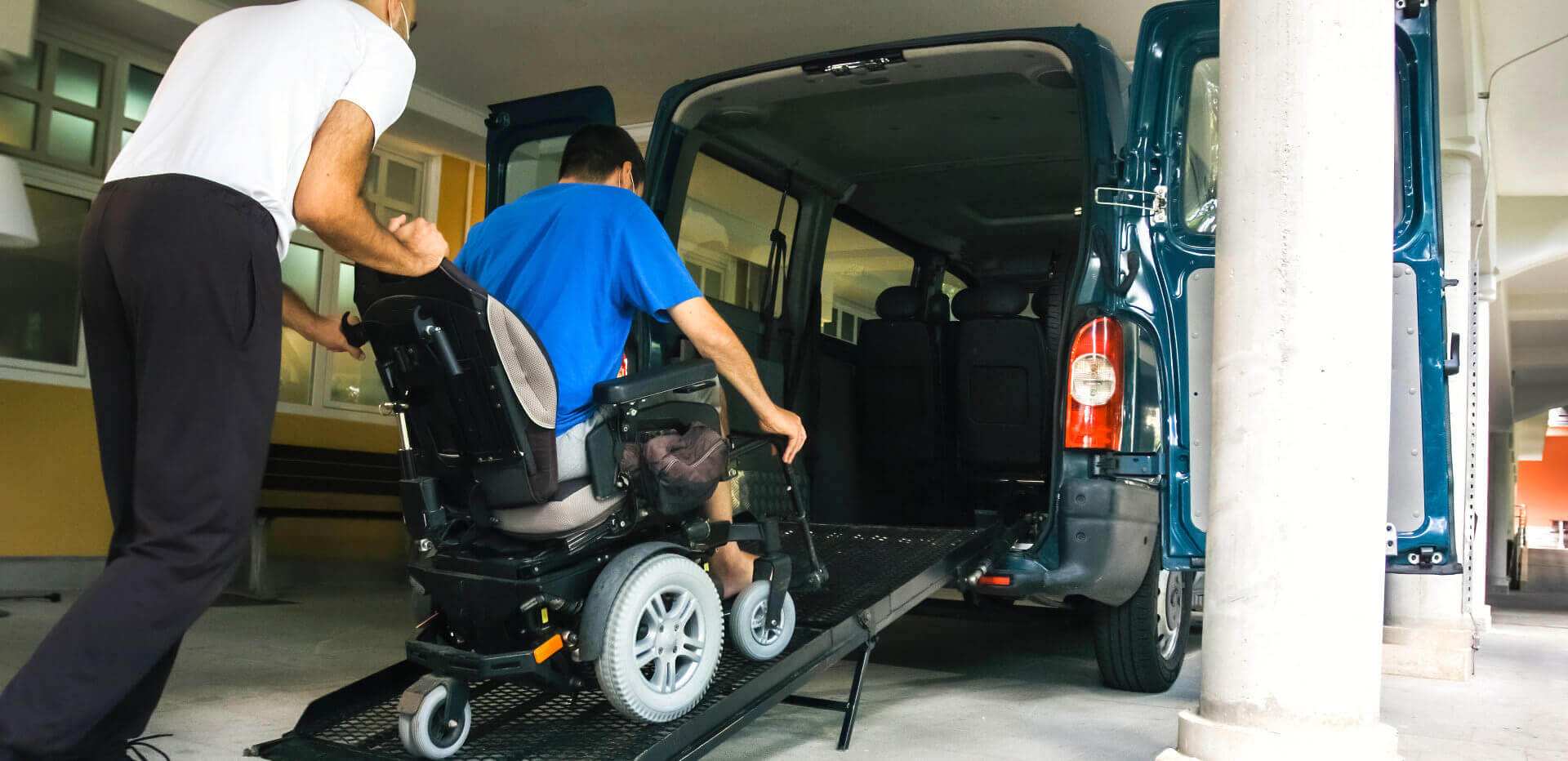 man assisting a person in a wheelchair to get on the car
