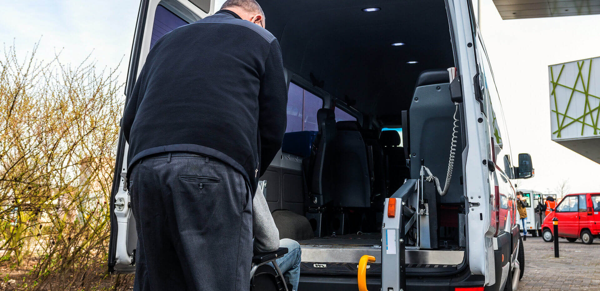 man assisting a person in a wheelchair to get on the car